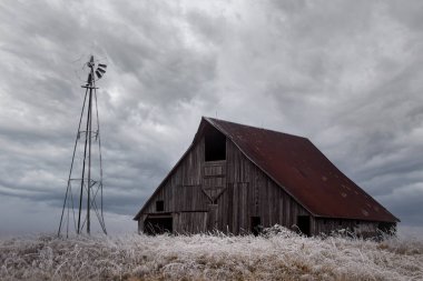 Eski bir ahır ve arkasında güzel bir gökyüzü olan buzlu bir yel değirmeni.