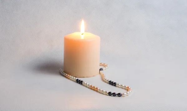 Burning candle and round white pearl beads — Stock Photo, Image