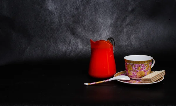 Αντίκες φλιτζάνι και πιατάκι και το γάλα σε ένα γυάλινο βάζο πορτοκαλί και γκοφρέτα — Φωτογραφία Αρχείου