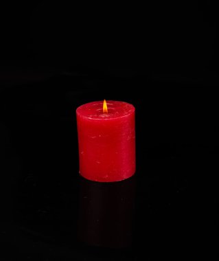Tek bir yanan kırmızı mum siyah arkaplanın önünde izole edilmiş.