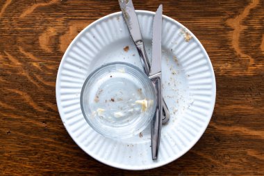 Tırtıklı ve tereyağlı ekmek kırıntılarıyla kaplı pis bir seramik tabağın yanı sıra altında tereyağı olan küçük bir cam kase. 2021 Şubat 'ında, koyu ahşap bir yemek masasında yatıyordu..