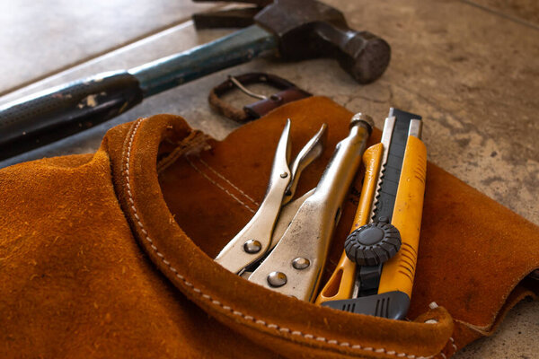 Home improvement tools in a suede tool belt. A multitool, a hammer, and a precision box-cutter knife with yellow edges.