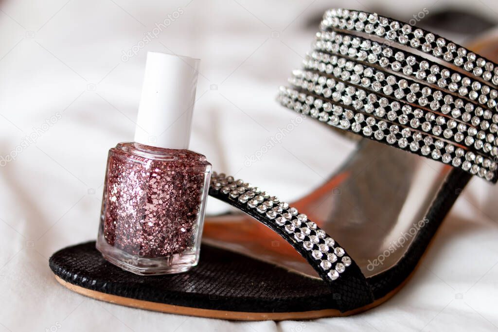 Soft-focus, glittery nail polish to match a glittery bedazzled two inch high heel shoe on a white bed sheet, isolated, Ontario Canada 2021.