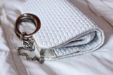 Beyaz örülmüş el çantası (çanta) gümüş bir toka ve zincir, açılı, yakın plan, beyaz bir yatak üzerinde, 2021.