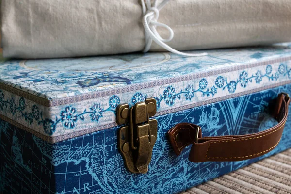 Closeup shot of vintage luggage with. a leather strap and brass buckle, topped with a rolled paintbrush carrier, blue design.