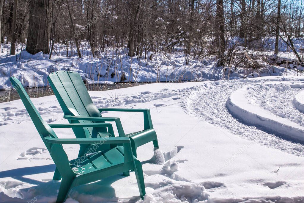 Turquoise Adirondack chairs in a snowbank in Southerwestern, Ontario, Canada along an icy creek, 2021.