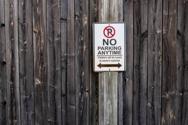 A vertical and rectangle shaped no parking anytime sign is tacked up to a weathered wooden fence in London, Ontario, Canada, February 2021.  