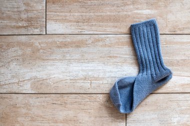 A single ribbed mid-calf blue wool sock that is missing its partner lies on a gold-beige tile floor bathed in sunlight in Toronto, Ontario, Canada, February 2021.