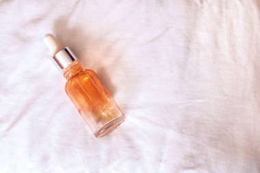 An empty serum bottle with an orange tint and white dropper head, slightly unscrewed, on a white fabric, isolated, in Canada during the wintertime 2021.