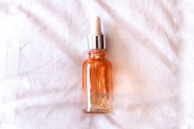 An empty serum bottle with an orange tint and white dropper head, slightly unscrewed, on a white fabric, isolated, in Canada during the wintertime 2021.