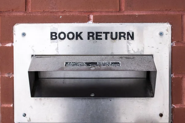 An old, weathered, aged metal book return container in a brick wall in downtown London. Reading books during the COVID-19 pandemic, high-volume checkouts and holds.