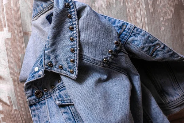 Closeup of a denim jacket folded in half on a gold bed spread. Jacket has silver buttons, faded blue jean look, Ontario, Canada.