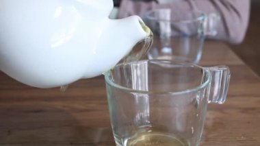 Elinde seramik çaydanlık tutan bir kadın, temiz yeşil çayı dökerken aynı zamanda, küçük bir kafede bardağa, uzun bir bardağa dökmeye çalışıyor. Arkaplan olarak ahşap masa.