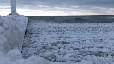 January 2021: Large chunks of frozen ice water lap against the pier at Grand Bend Beach (Lake Huron), Lambton Shores, Ontario, Canada.