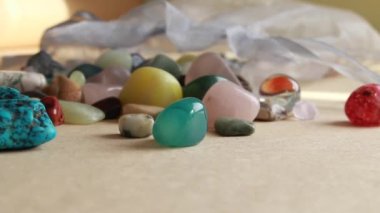 A hand grabbing a stone from a gem stone collection inside a pale blue silk sachet spilled onto a beige background, Ontario, Canada, 2021.
