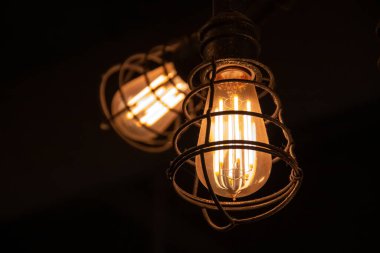 Londra, Ontario, Kanada 'da Mart 2021' de bir barın tavanından sarkan demir bir kafesin içinde parlayan liflerle parlayan parlak bir ampul..