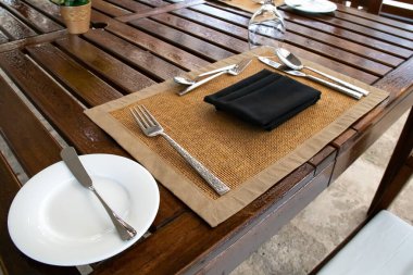 Maun ağacından bir masada kullanılmamış bir yer. Tereyağı bıçağı, çatal, kaşık, şarap kadehi baş aşağı, beyaz servis tabağı, siyah peçete. 2021 'de lüks bir Barbados restoranında vuruldu..