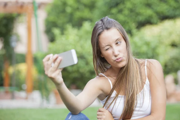 Close up portrait of a young attractive woman holding a smartphone digital camera with her hand and taking a funny self portrait — Stock Photo, Image