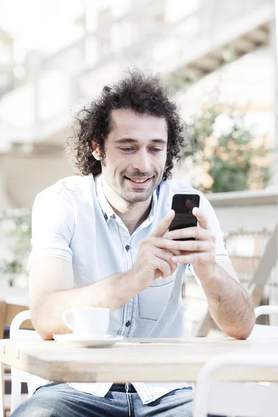 Handsome man watching social media in a smart phone in a restaurant terrace