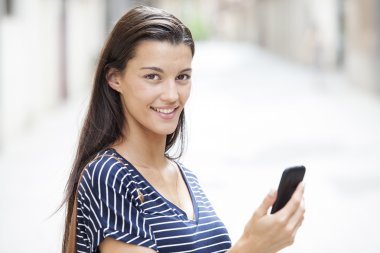 Sokakta odaklanmamış bir arka plan ile bir akıllı telefon kullanan mutlu kadın