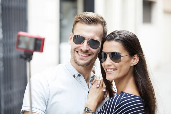 Alegre joven pareja haciendo un selfie con un teléfono inteligente y selfie stick —  Fotos de Stock