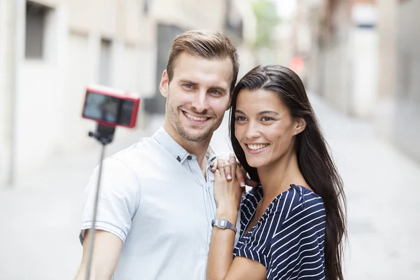 Alegre joven pareja haciendo un selfie con un teléfono inteligente y selfie stick — Foto de Stock