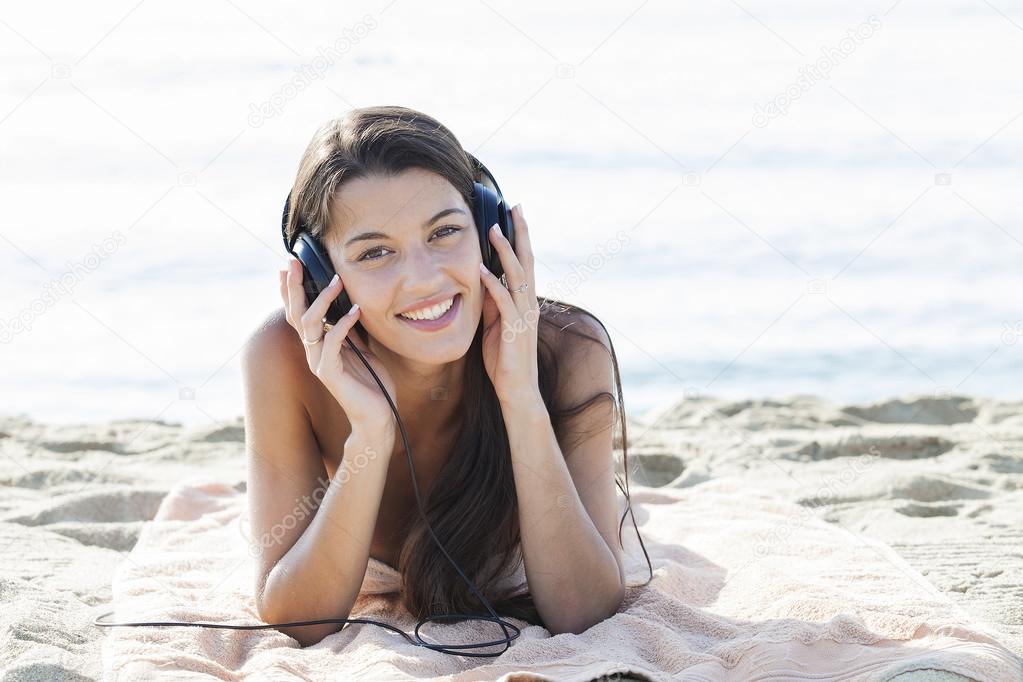 Young attractive woman listening to music on sand beach