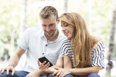 Çift bir parkta bir bankta oturan bir akıllı telefon medya paylaşımı