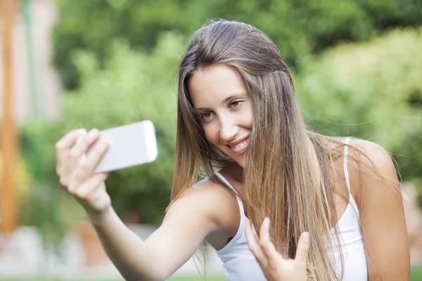 Menina sentada no parque e faz selfie, feliz — Fotografia de Stock