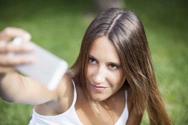 Girl sitting in the park and makes selfie, happy — Stock Photo, Image