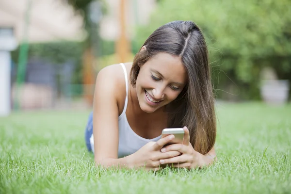 젊은 여 자가 잔디에 누워 있는 동안 휴대 전화를 사용 하 여 — 스톡 사진