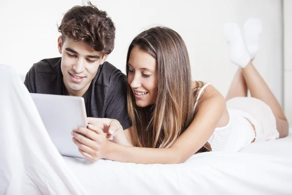 Feliz hermosa pareja joven acostada en la cama usando una tableta digital —  Fotos de Stock