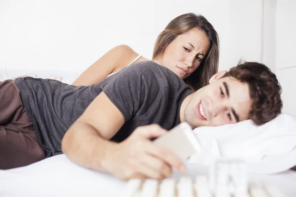 Žárlivý drby manžel sleduje jeho manželka mobilní telefon na postel — Stock fotografie