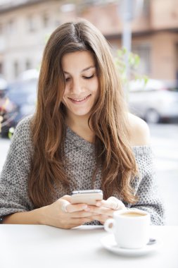 Teras barda oturmuş ve cep telefonu tutarken gülümseyen güzel kız