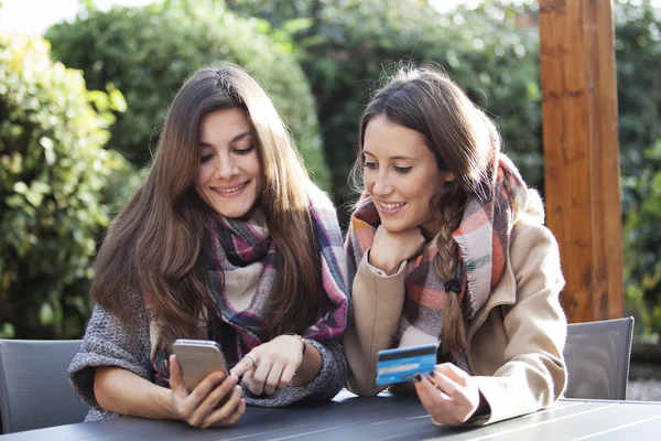 Two young friends shopping online with a credit card and a phone