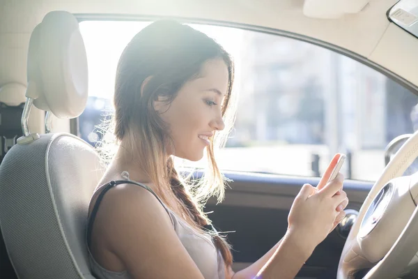 Mujer joven enviando un mensaje con su teléfono móvil sentado en su coche — Foto de Stock