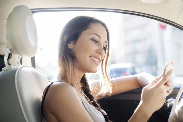 Mujer joven enviando un mensaje con su teléfono móvil sentado en su coche — Foto de Stock