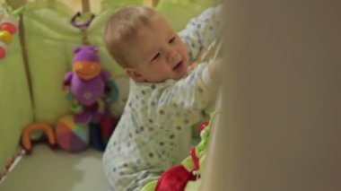 Kameraya bakarak beşik ayakta şirin bebek çocuk evde, yürüyüş ve oyuncaklarla oynamak