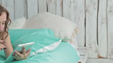 Tablet pc ile yatakta yatan genç kadın kıvırcık. Dolly vurdu