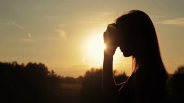 Kadın bir sanal gerçeklik gözlük ormanda günbatımında kullanır