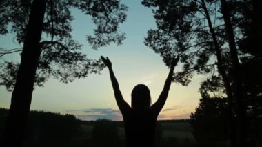 Mutlu genç kadın silueti gökyüzüne karşı ellerini havaya kaldırdı