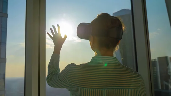 Woman silhouette using VR headset against skyscraper window