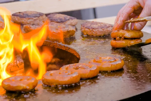 Шеф-повар жарит свежие свиные колбаски на жаровне с горячим пламенем — стоковое фото