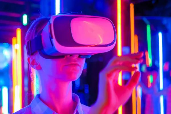 Young woman using virtual reality headset at dark interactive VR exhibition