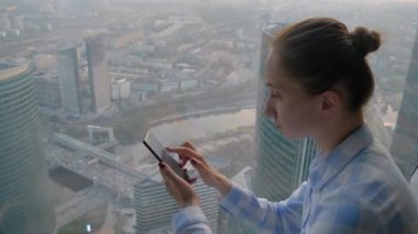 Gökdelen penceresinden şehir manzarasına karşı akıllı telefon kullanan kadın