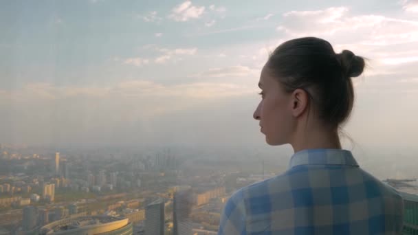 Back view of woman looking at cityscape through window of skyscraper — Stock Video