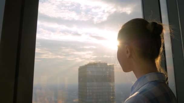 Woman looking at cityscape through window of skyscraper - sun lens flare — Stock Video