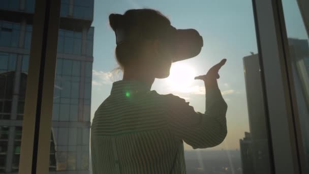 Медленное движение: женщина, использующая VR гарнитуру против окна небоскреба в офисе — стоковое видео