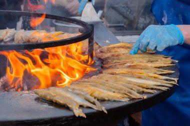 Aşçı yemek festivalinde siyah brazier üzerinde un kokulu balık pişiriyor.