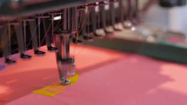 Kırmızı kumaş üzerinde sarı Nike logosu yapan nakış makinesi